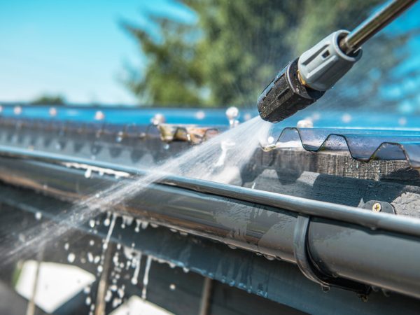 Spring Rain Gutters Cleaning Using Pressure Washer. Closeup Photo.